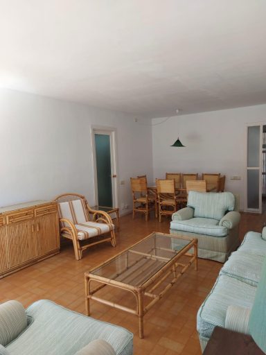 Sala de estar luminosa con muebles de madera y sillas de color claro. Mesa en el centro.